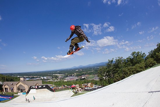 Snowboarder jumps high on snow-covered mountain with green hills in background