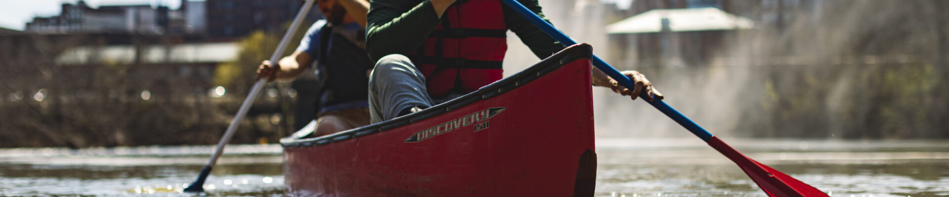 Men canoe with a city skyline in the background