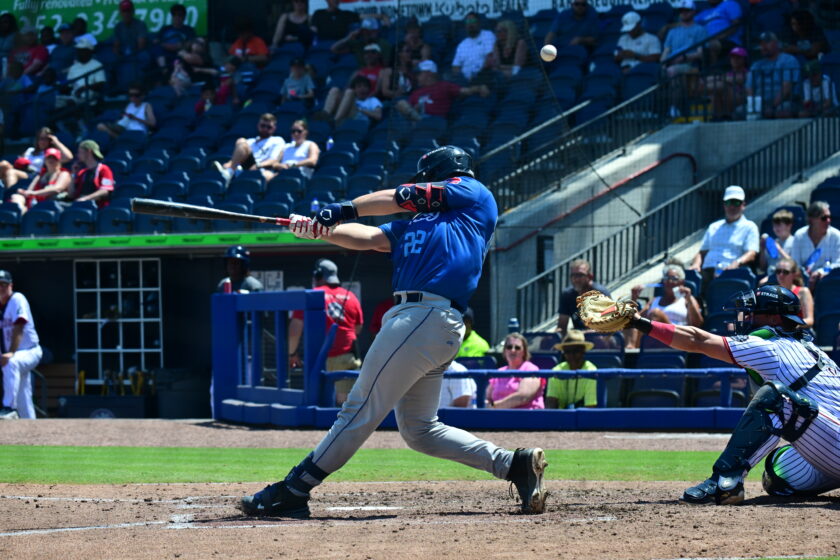 Baseball player swings at bat in a stadium with crowd looking on