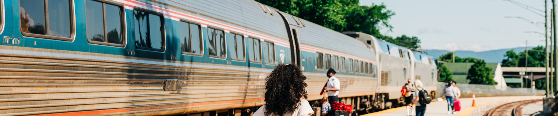 Woman in red skirt walks toward Amtrak train with luggage