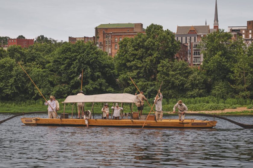 Rowers dressed in old-fashioned gear row a batteau down a river
