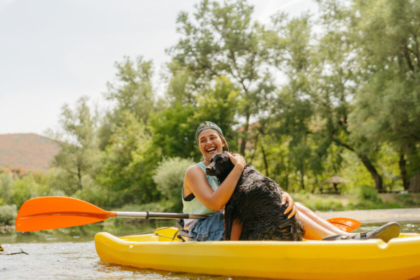 Photo of a young woman kayaking down the river and enjoying nature with her dog.