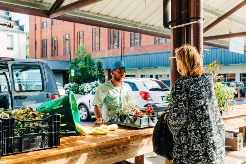 Produce vendor speaks with female shopper at a market