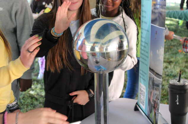 Close-up of a silver ball and students in the background watching an experiment.