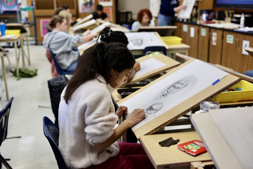 Middle School students sit in a row sketching on art boards.