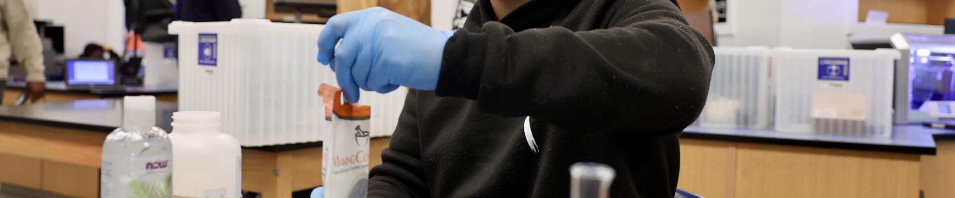 Male student adding product to a container while smiling at the camera