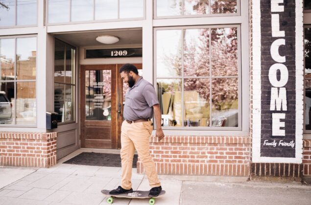 Black male on skateboard in front of brick storefront