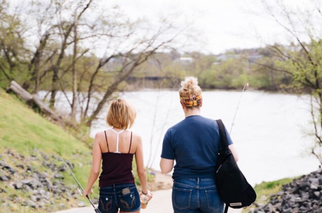 Two women with fishing rods walk toward lake