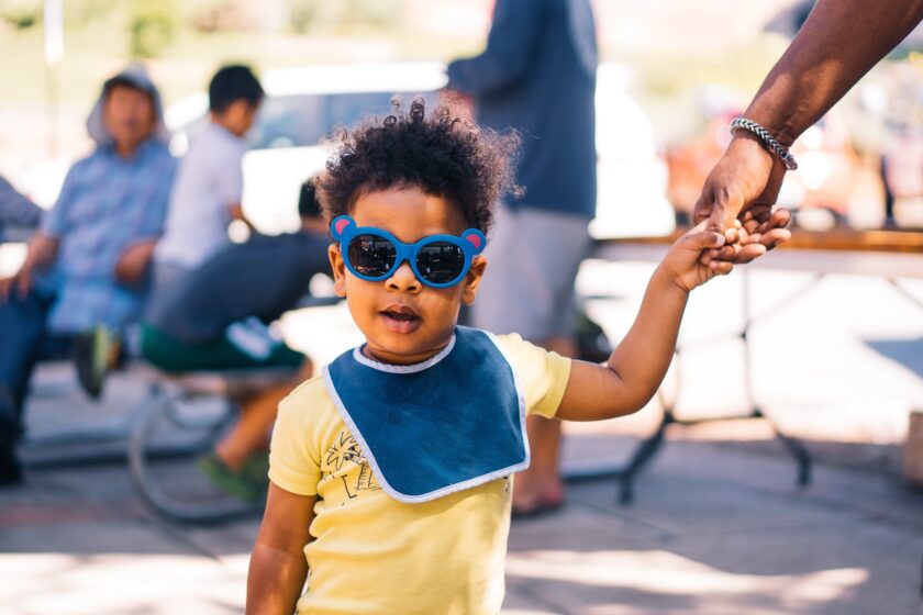 BIPOC young boy in sunglasses and a yellow t-shirt holding a hand
