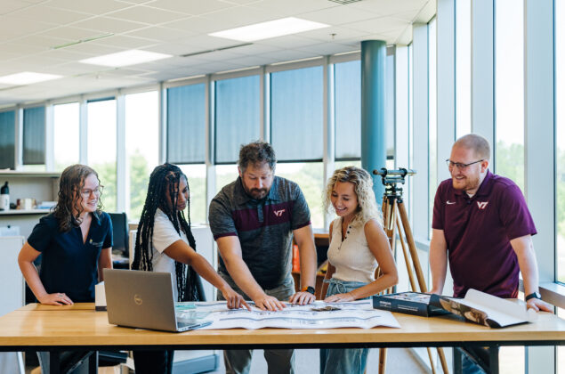 Young professionals stand around a desk engaged and pointing at documents.