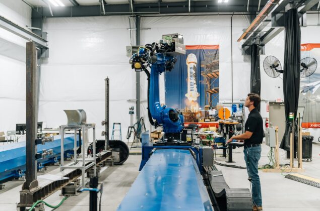 Young male employee stands in front of robotics machine in an aerospace manufacturing facility
