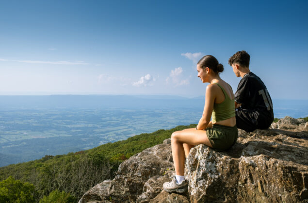 "Teenage siblings sitting on the mountain ridge enjoy the view of Shenandoah National Park "