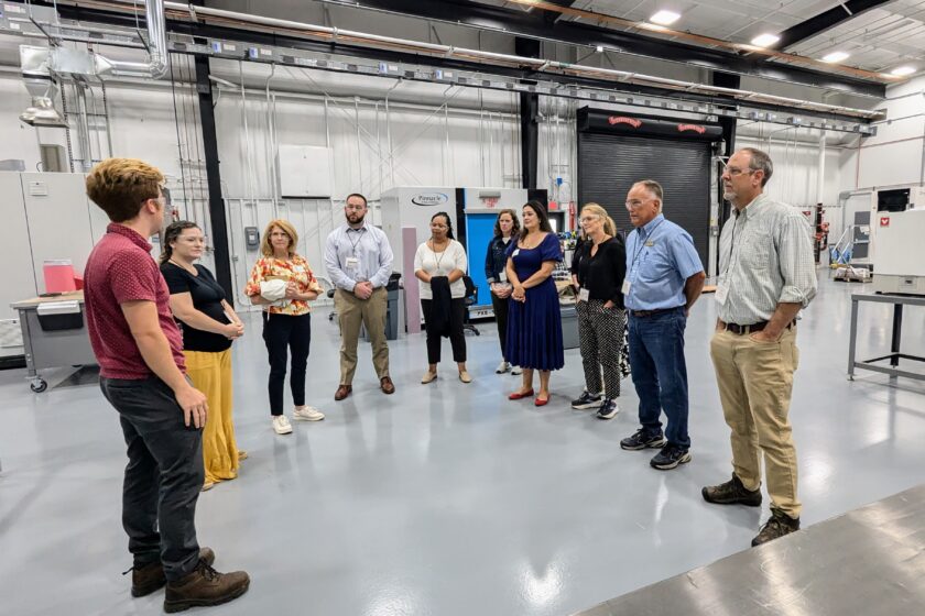 Educators stand in circle listening as factory employee speaks
