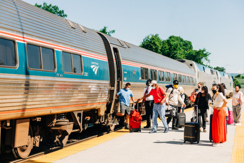 People on an outdoor train platform board a train.