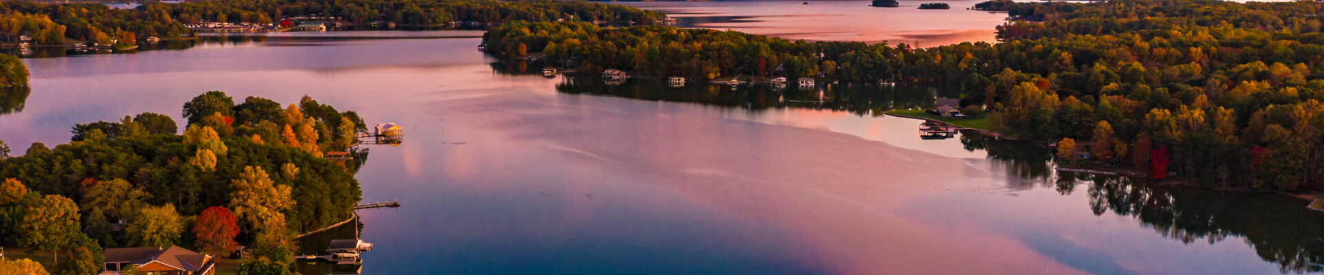 Large lake surrounded by forest and mountains in the background, houses dotted along the shore with private docks