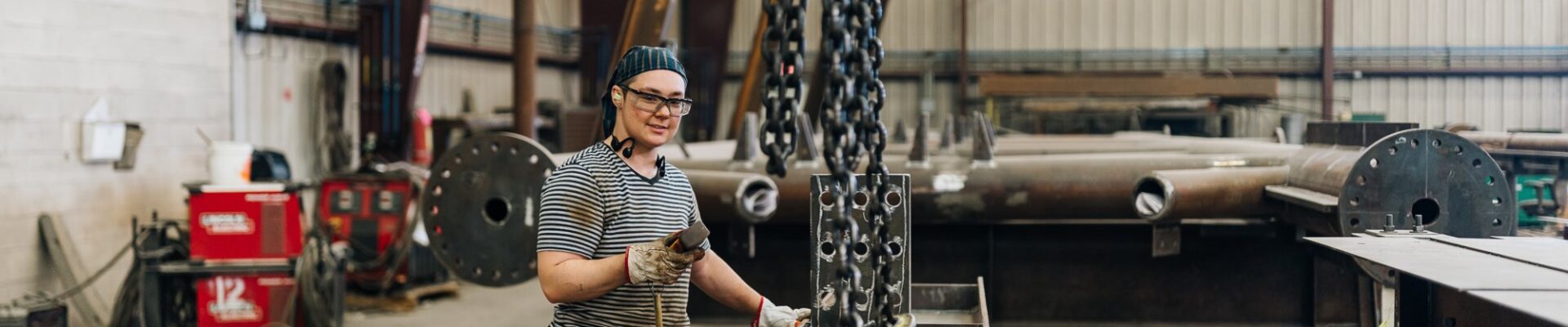 A worker stands alongside heavy metal chains in a factory.