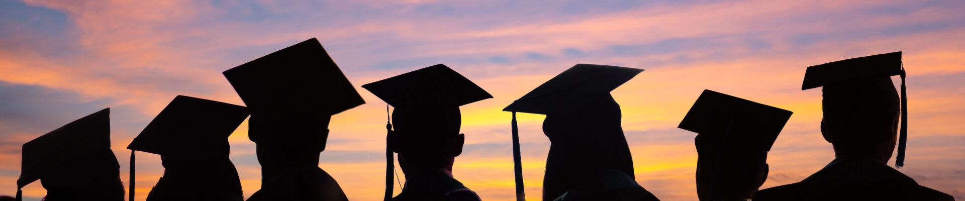 Silhouettes of students with graduate caps in a row on sunset background.