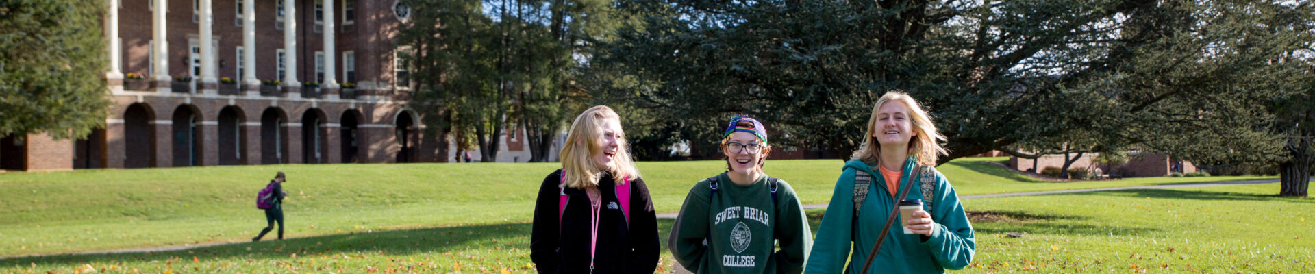 Three college students laughing as they walk across a campus quad