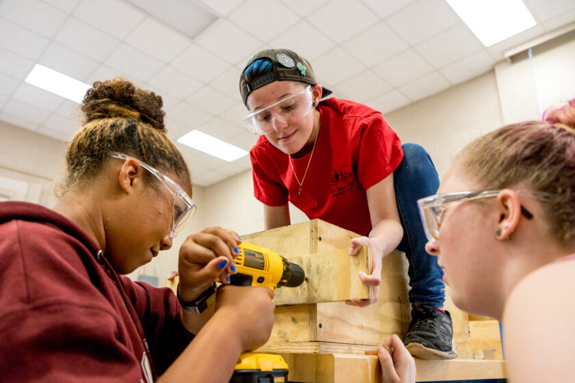 Three young students drill wood for a project togther