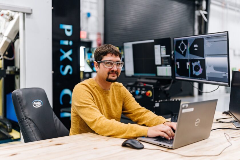 Engineer working on a laptop in an industrial facility with CAD software displayed on multiple monitors
