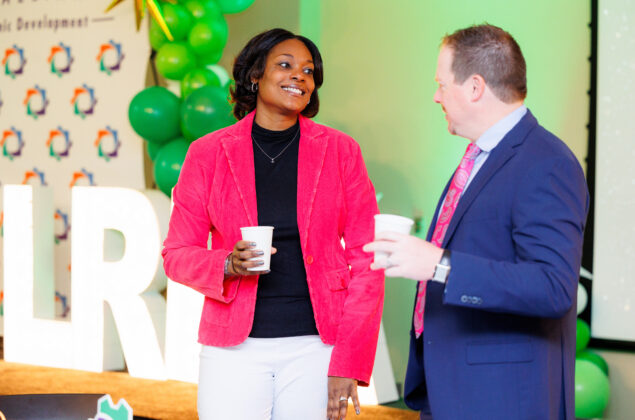 A businesswoman speaks to a businessman while at a business event.