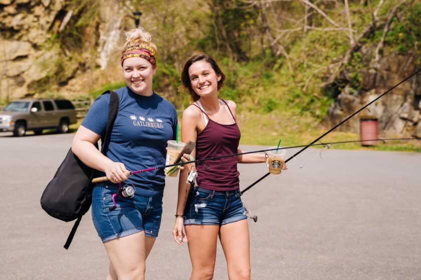Two women carry fishing poles outdoors.
