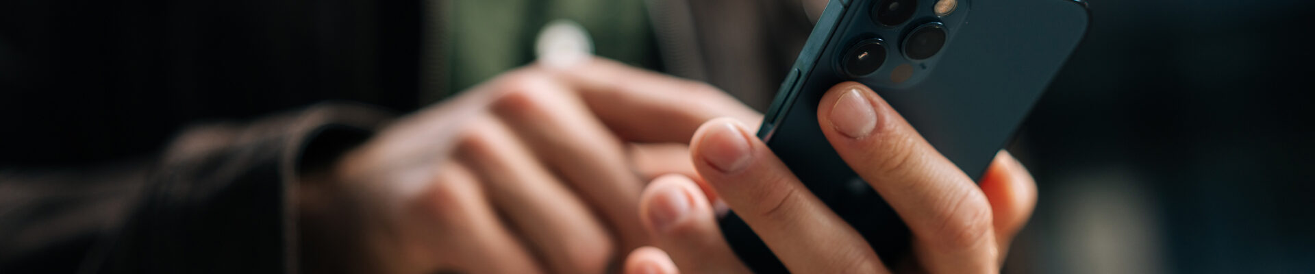 Close-up hands of unrecognizable man holding and using smartphone standing on city street, browsing internet, checking social media, using mobile application. Concept of modern communication.