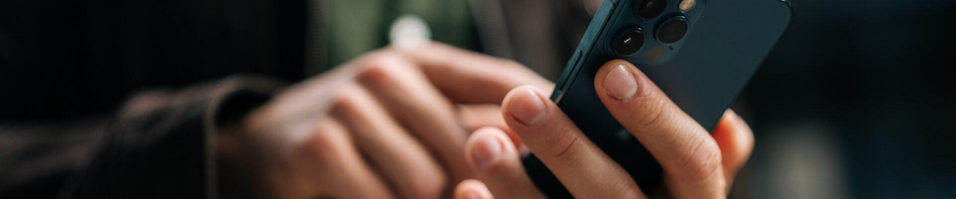 Close-up hands of unrecognizable man holding and using smartphone standing on city street, browsing internet, checking social media, using mobile application. Concept of modern communication.